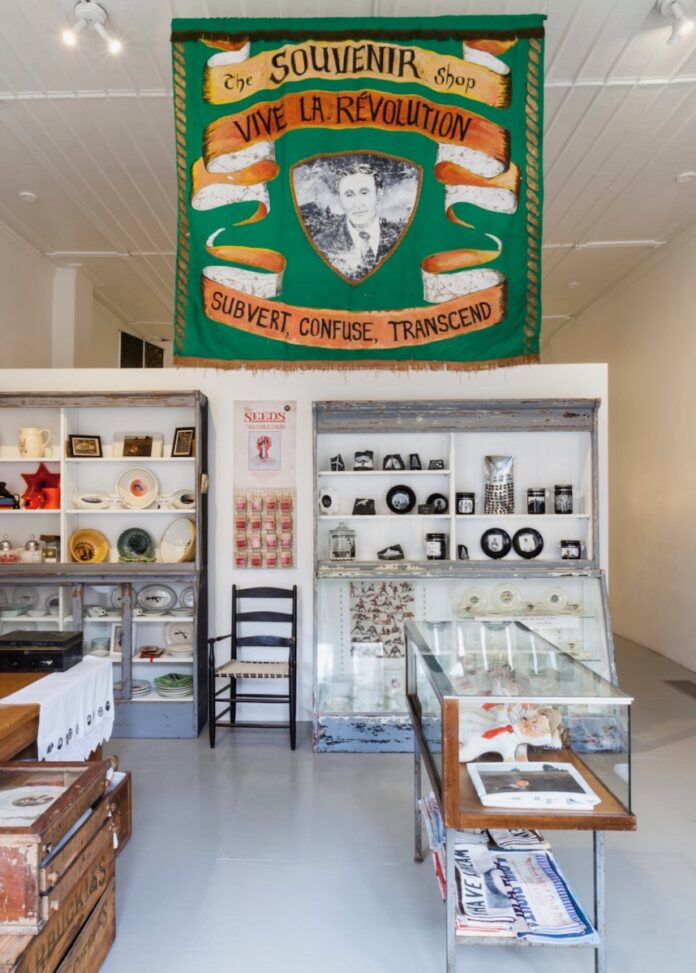 The inside of the Mattress Factory Gift Shop for the museum with white shelves and a green banner.