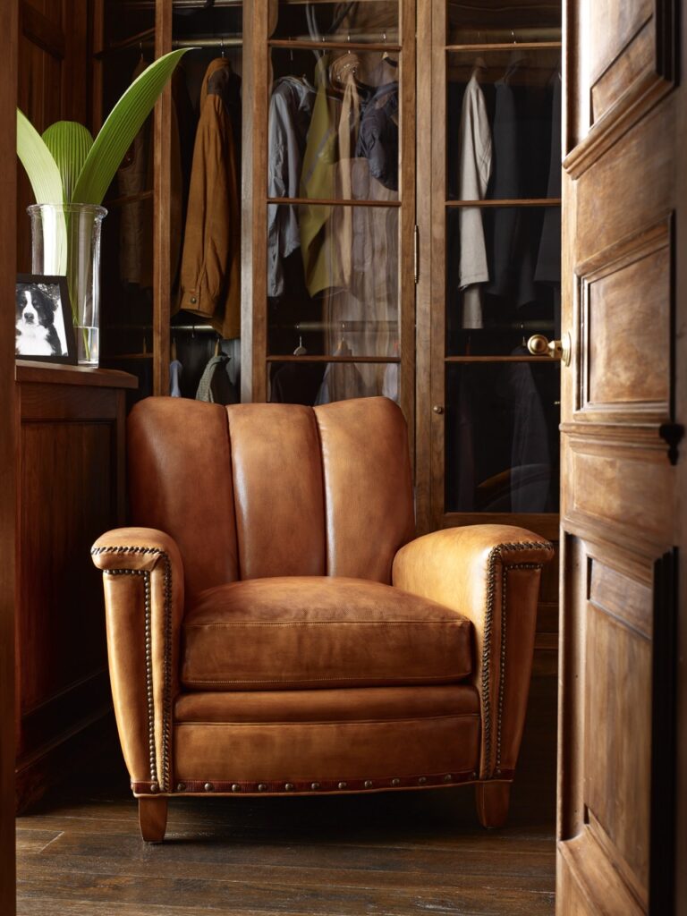 A brown leather chair sits in a naturally lit living room set up with a closet behind the chair and door to the right.