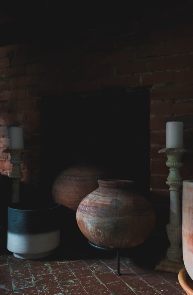 Various sizes of pottery from large circular shapes to plant pot shapes sit in a darkly lit brick road and brick doorway.