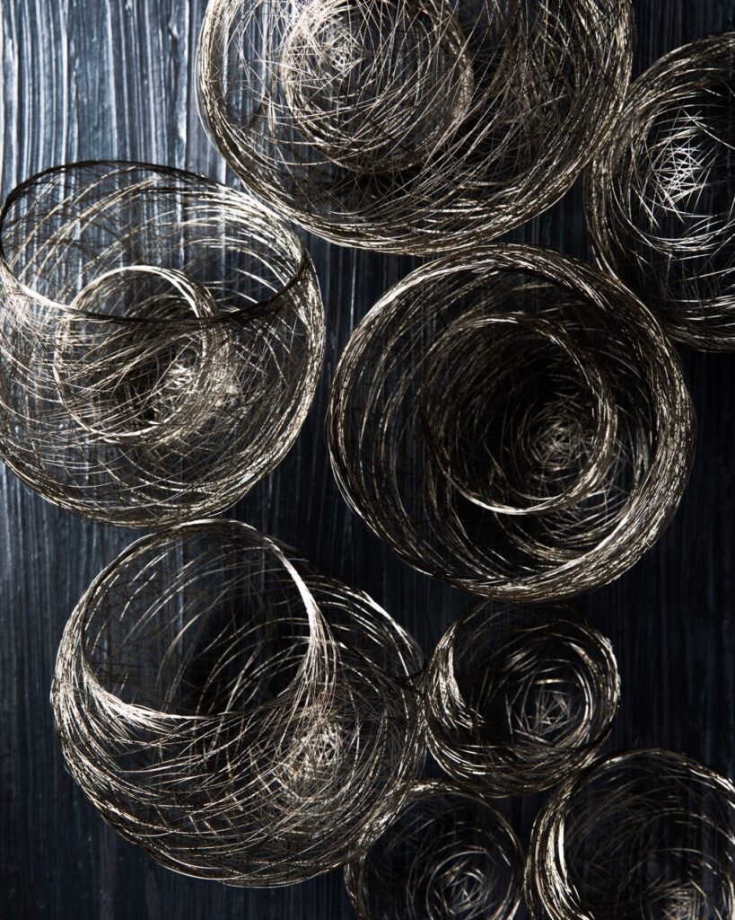 8 light brown, wire-type baskets sit scattered amongst a black table.