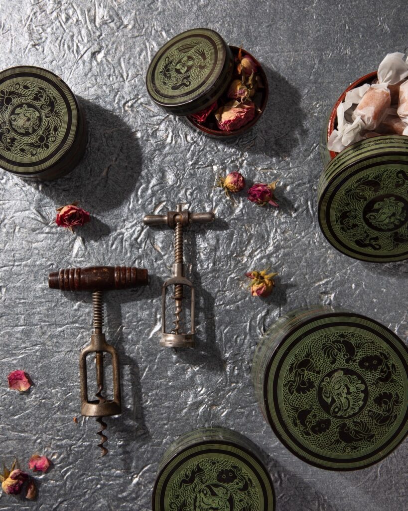 Little green jars of dried flowers and tea sit out on a grey table with two wine bottle openers sitting in the middle.