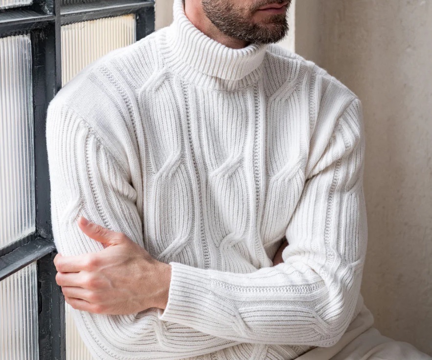 A man with his arms crossed wears a men's white turtleneck knit sweater.