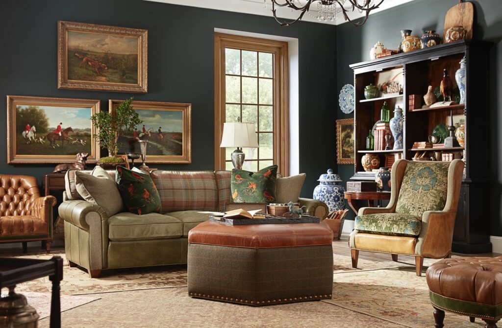 A large brown couch and ottoman with an orange leather top sit in a living area with dark walls filled with paintings.