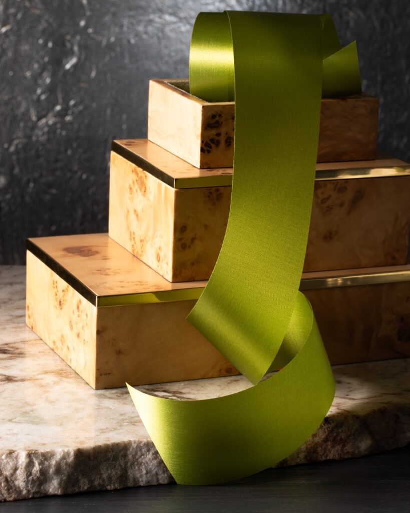 A set of natural good boxes with gold embellishments sit in a stack as a wide green ribbon runs down them.