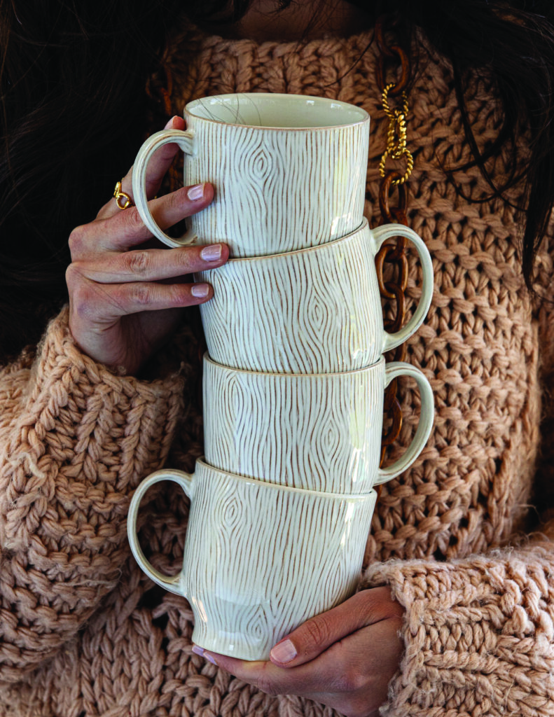 Four speckled mugs stacked on top of each other help by a woman in a sweater.
