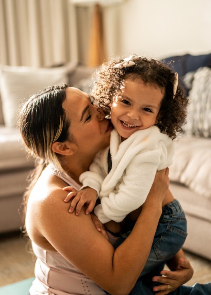 A mom holds and kisses her little girl in who is in a white fuzzy jacket.