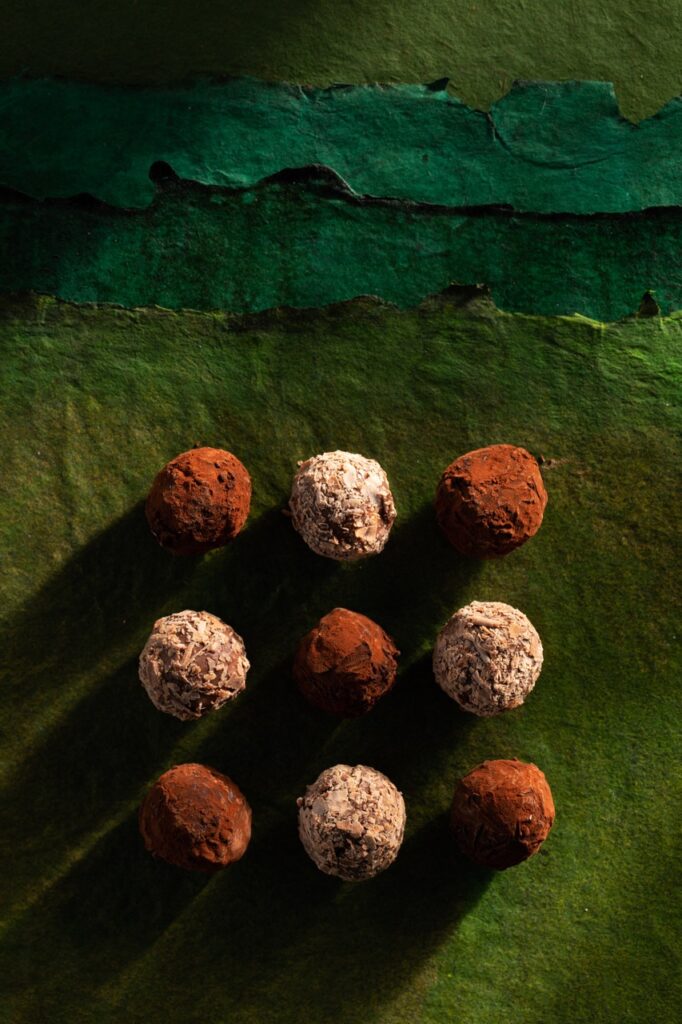 On top of green paper sits 9 chocolate truffles in light brown and white.