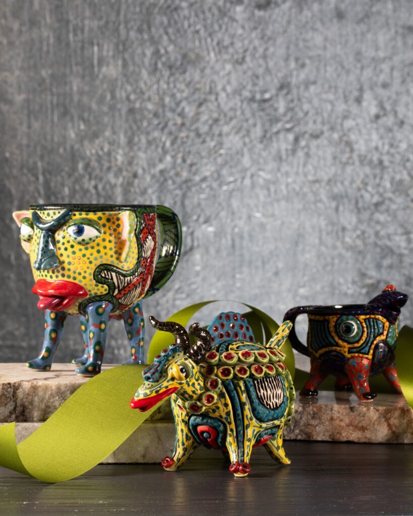 Three animal figures with bold colors and print and mug handles sit on concrete blocks in front of a grey background.