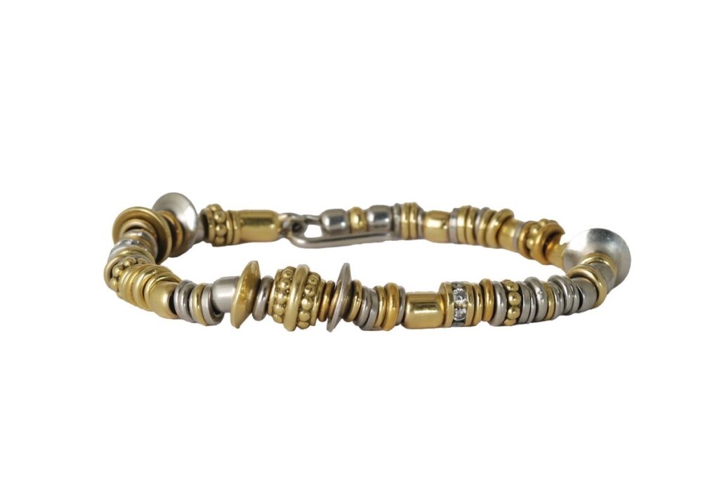 A womens bracelet made of gold and silver small round pieces sits on a white background.