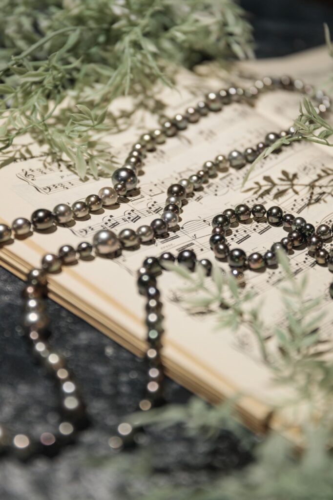 Two large metallic pearl women's necklaces sit on a piece of sheet music with pine branches on the edges.