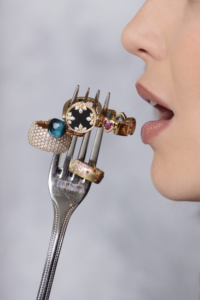 A woman holds a fork up to her mouth that has four golds rings sitting on it.