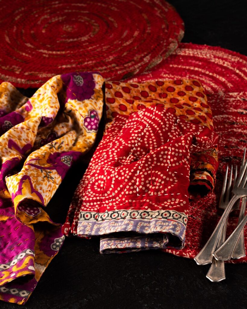 Red and purple scarves sit on a table with two red round wire plates beneath them.