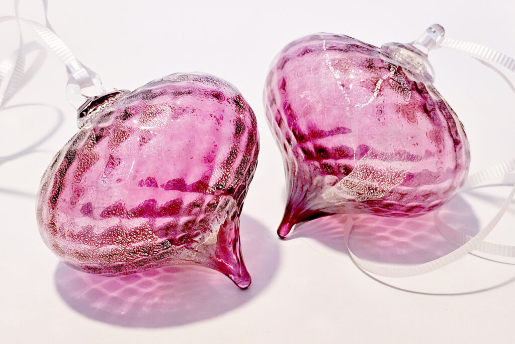 Two pink patterned glass ornaments that come to a drop shape at the bottom.