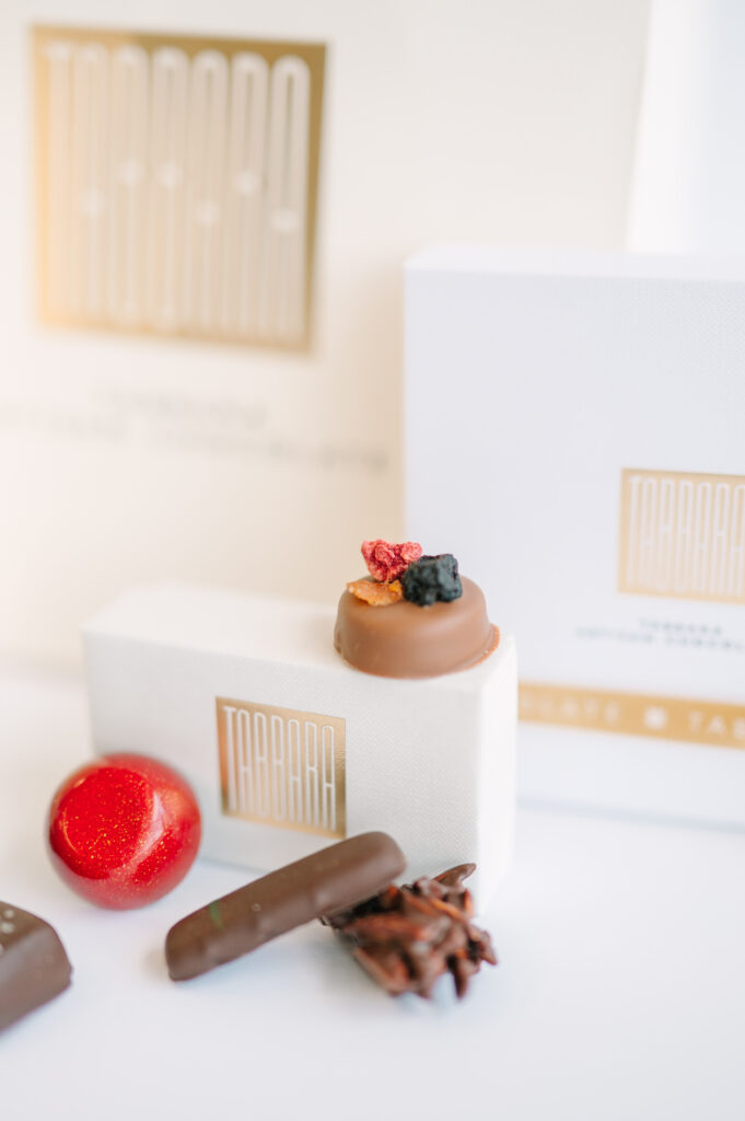 A variety of small chocolates are laid out on a table with a box in the back.