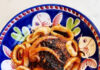Celebrate the Feast of the Seven Fishes in Pittsburgh A dish. of octopus and pasta prepared on a blue plate with floral designs on it.