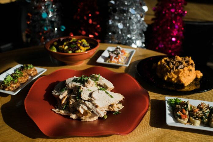 A variety of holiday dishes from Square Cafe. in Pittsburgh, like turkey and other sides sit on a wooden table in front of various colored Christmas trees.