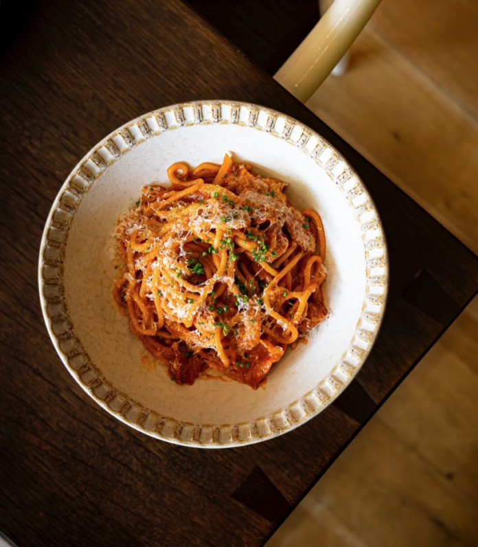 A white dish of spaghetti with red sauce on a brown table in Fish nor Fowl, Pittsburgh Italian restaurant.