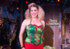 Pittsburgh Happenings: December 19-25 A woman in red and green Christmas attire and bushy blonde hair stands on a stage with a grin on her face.