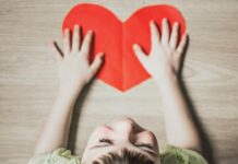 Family-Friendly Valentine’s Day Events in Pittsburgh A boy lays on a wood floor with a Valentine's Day red paper heart cut out in front of him.
