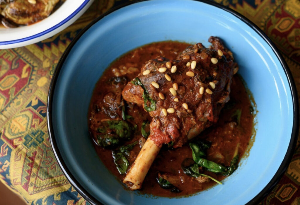 A blue bowl holds a dish of meat on a bone in a broth with plenty of herbs from Khalil's in Pittsburgh