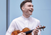Last Minute Tickets in Pittsburgh: January 22-28 A man in a white dress shirt holds a violin, smiling in front of a blue background.