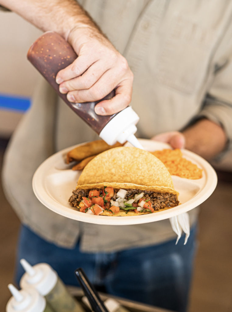 A man holds a plate of tacos as he squirts a sauce onto each of them at Pittsburgh best restaurants event.