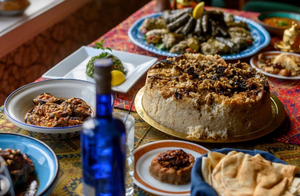 A spread of Syrian food on various plates sits on a red table with a blue bottle sitting amongst the plates.