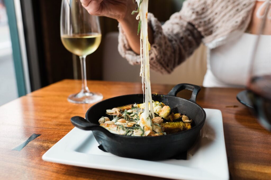 A person picks up a cheese pull from a small Valentine's Day cast iron pan of muscles as a glass of white wine sits nearby.