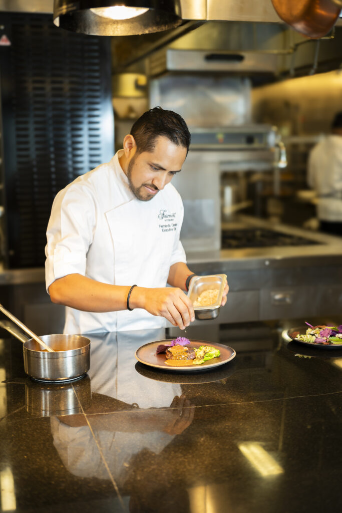 Chef Canales adding spices to a plate of food in the fairmont kitchen.