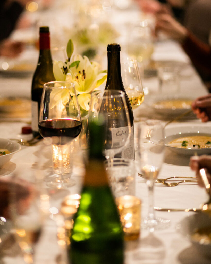 A table setting shows three bottles of wine, many wine glasses, and placemats set across it.