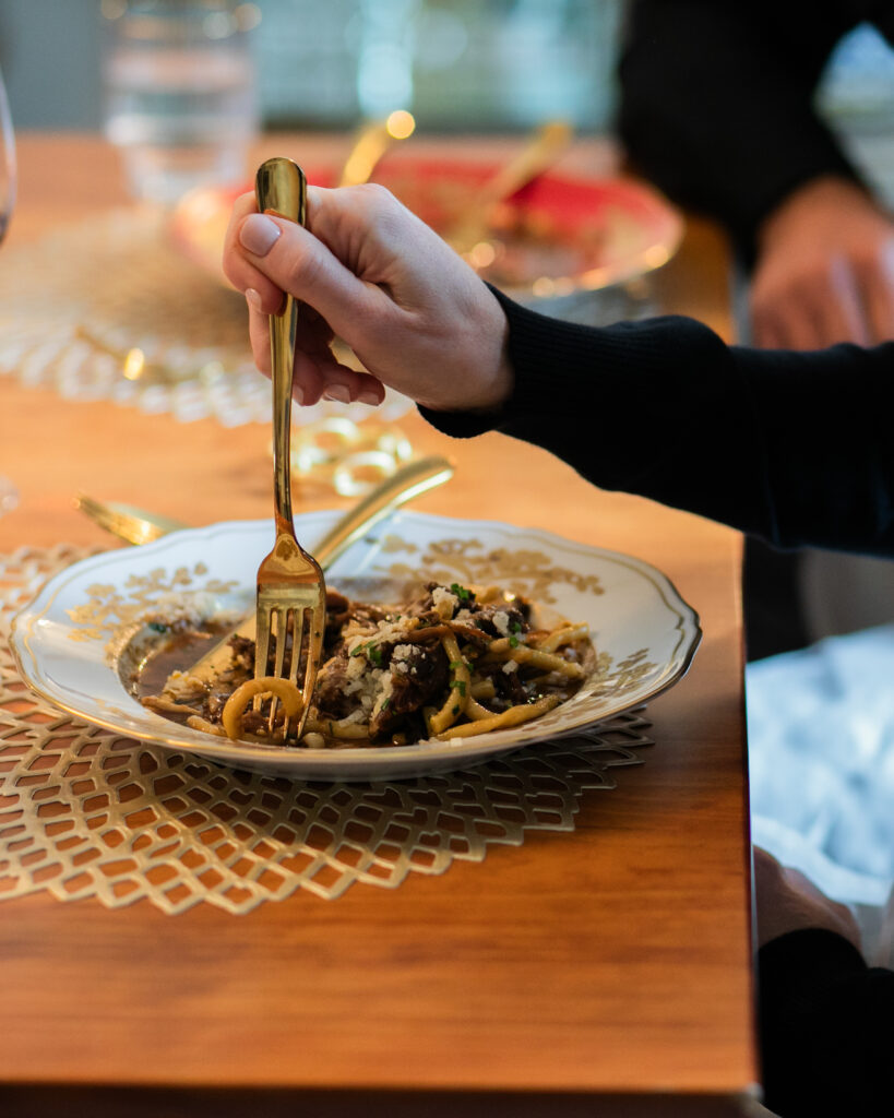 A person stabs their fork into a white plateful of spaghetti with gold embellishments around the rim of the plate at a tasting of Il Borro Tuscany Wines.