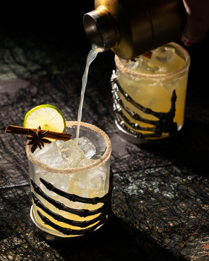 Apple cider margarita with a cinnamon sugar rim and lime garnish in a Halloween-inspired glass.