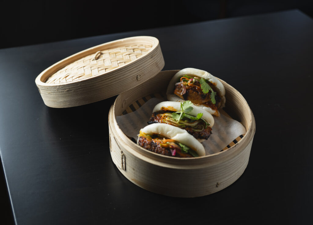A basket of three pork belly buns on a black table