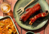 Soul Food Restaurant Cuddy’s to Open at Lawrence Hall Two green pans hold pepper steak and oxtails while a green plate holds a rack of ribs and a fork. Dipping sauces and a beer sit to the left all from Cuddy's Restaurant at Lawrence Hall.