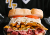 Embrace Your Pittsburgh Spirit at Yinzerfest 2024 A Pittsburgh hockey player holds a Pittsburgh-style sandwich in his gloves stacked high with french fries, meat, and coleslaw.