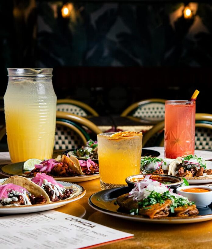 Cinco de Mayo Specials at Pittsburgh Restaurants Three drink glasses in yellow and orange and red sit amongst a table of tacos on various plates with a menu sitting in the bottom left corner for a Pittsburgh Cinco de Mayo celebration.
