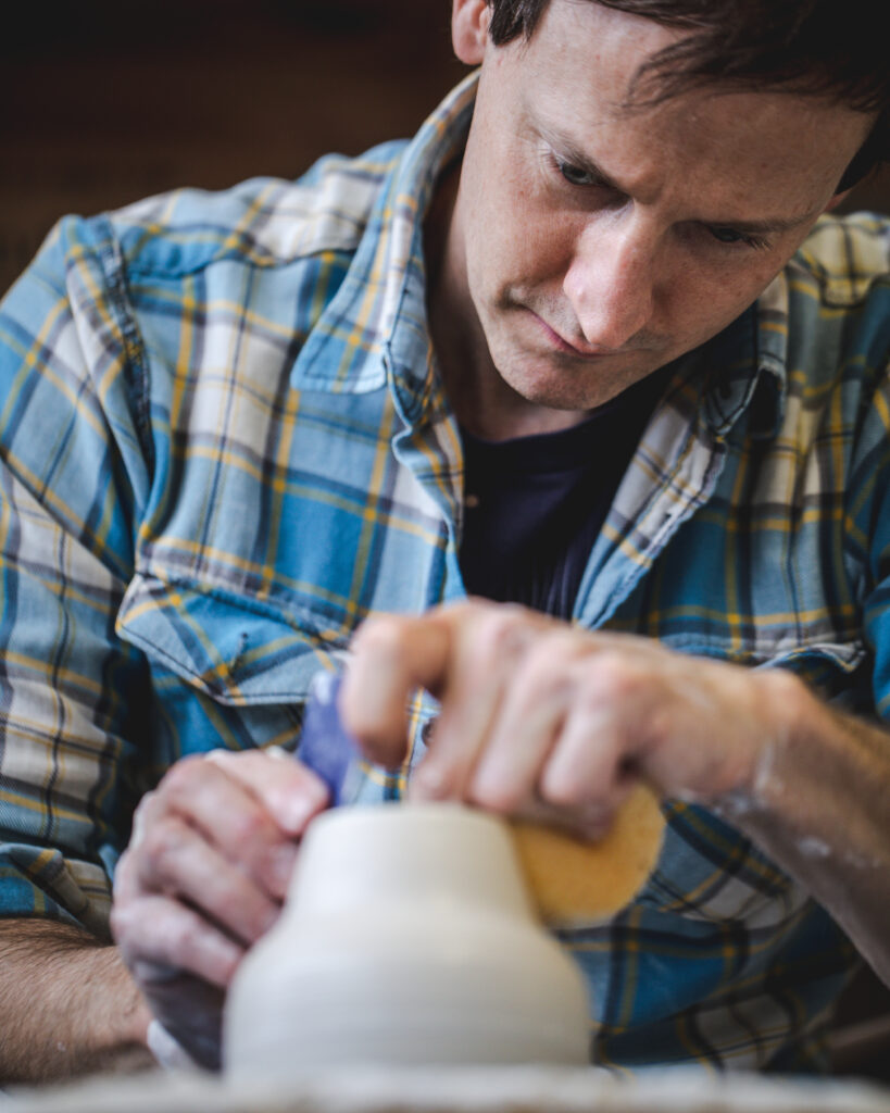 Ceramic Artist Andrew Jowdy Collins forms a piece of clay with a shaping tool to make a vase.