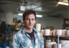 Ceramic Artist Andrew Jowdy Collins Shares His Story Ceramic artist Andrew Jowdy Collins stands in his studio work table with a ceramic mug being made in the process in front of him.
