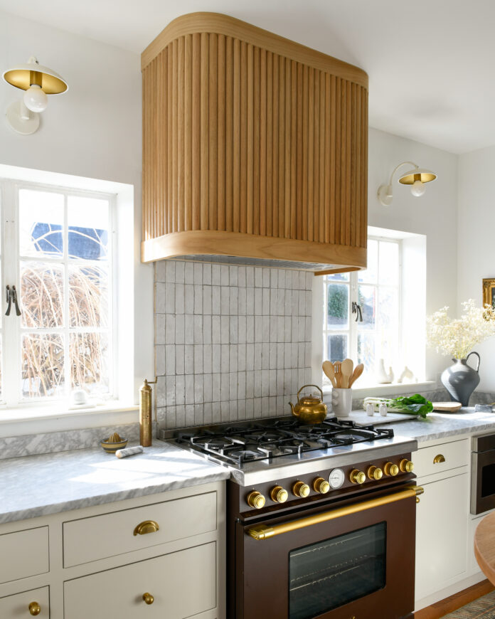 Remodeling a Small Town Kitchen for a Big City Feel A picture of a black stove with gold embellishments in a remolded kitchen featuring a wooden hood above the stove and tiled backsplash.