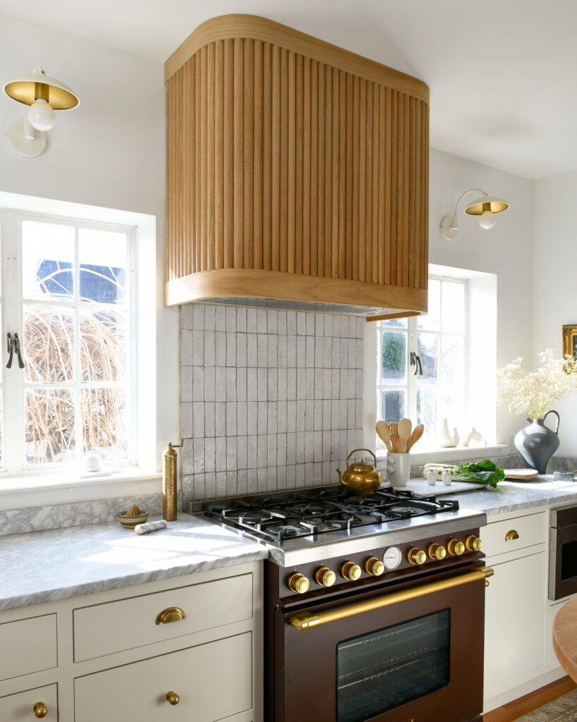 A picture of a black stove with gold embellishments in a remolded kitchen featuring a wooden hood above the stove and tiled backsplash.
