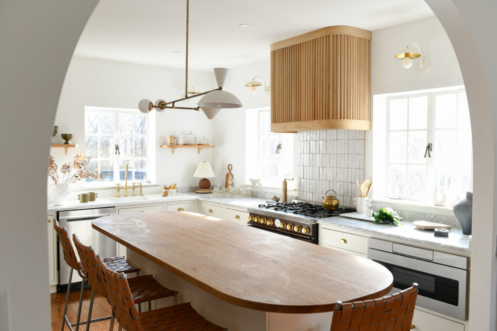 A shot of a kitchen interior after remodel with a brown oval table in the center alongside white countertops and walls.