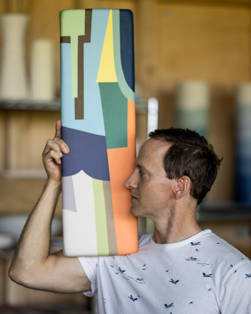 Ceramic Artist Andrew Jowdy Collins holds a multi-colored block painting on his shoulder in his Pittsburgh studio.