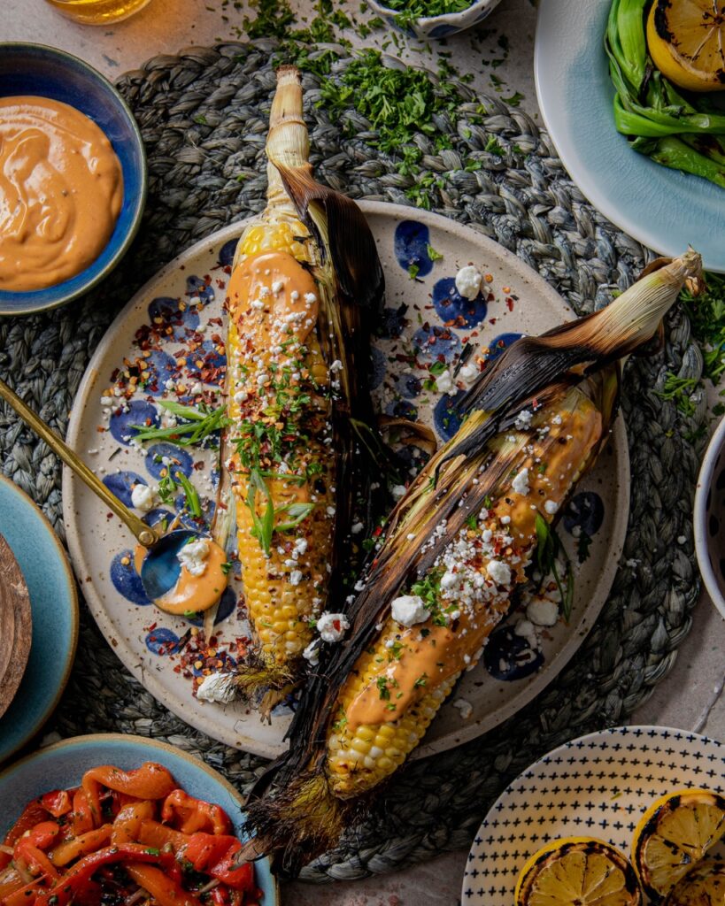 A plate holds two ears of corn from off the grill with seasonings and cheese sprinkled on top.