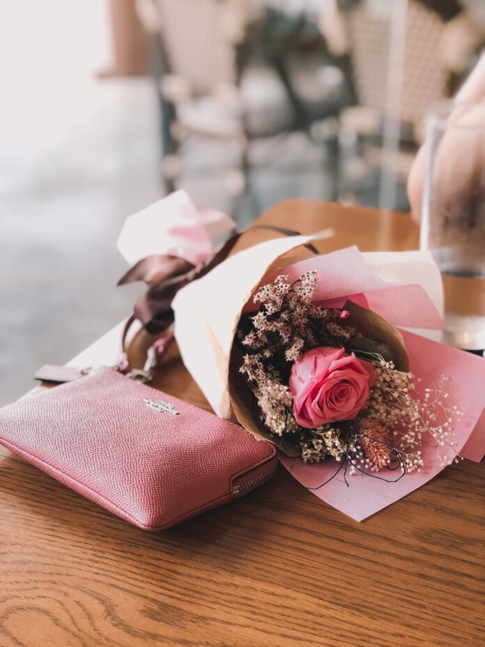 A purse and a bouquet of flowers sit on a wood table for Mother's Day gifts.
