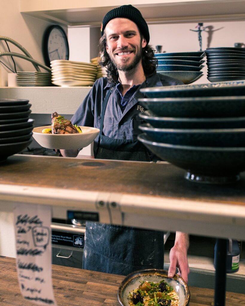 A man stands behind the counter at an allergen-sensitive eatery in Pittsburgh, a plate in his hand that he's ready to serve.