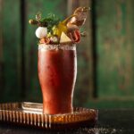 An antipasto virgin non-alcoholic bloody mary with various antipasto garnishes like cocktail onions, olives, cheese slices, and salami.