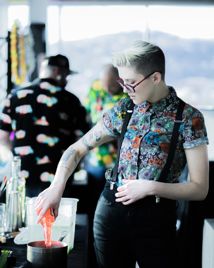 A person in a patterned dress shirt pours an orange soda into a pot.