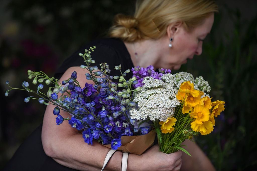 A woman at the Greater Pittsburgh Flower Collective carries a bundle of flowers in her hand in yellow, purple, and white.