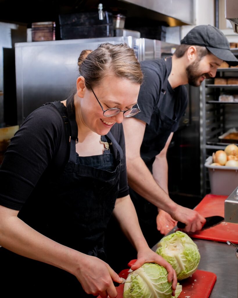 Two members of Apteka cook up a plant-based meal out of cabbages for the community of Pittsburgh.