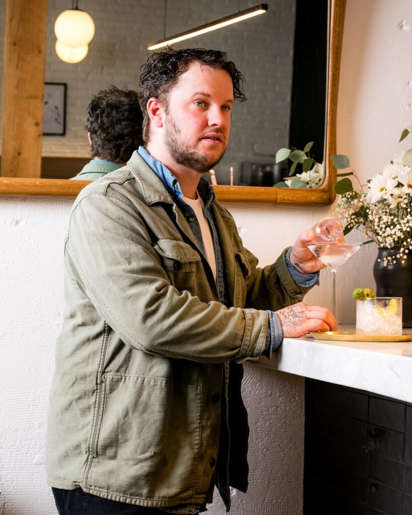 Joey Hilty, a risk taker in Pittsburrgh stands at a bar with a martini glass in front of him.